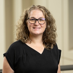 Image of Adriene Beltz. Woman wearing black shirt, standing in front of neutral background.